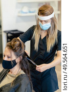 Hairdresser, protected by a mask, making waves in her client’s hair with a hair iron in a salon. Business and beauty concepts. Hairdresser, protected by a mask, combing her client’s hair with a hair iron in a salon. Стоковое фото, агентство Ingram Publishing / Фотобанк Лори