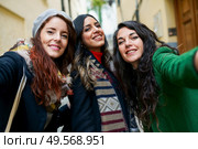 Multiethnic group of three happy woman taking a selfie photo with a smartphone in urban background. Group of three happy woman walking together outdoors. Стоковое фото, агентство Ingram Publishing / Фотобанк Лори