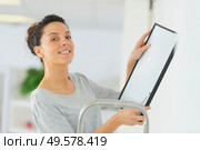 woman positioning picture frame on wall. Стоковое фото, агентство Ingram Publishing / Фотобанк Лори