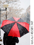 Woman holding a black and red umbrella under snow walking in a snowed street.. Woman holding a black and red umbrella under snow. Стоковое фото, агентство Ingram Publishing / Фотобанк Лори