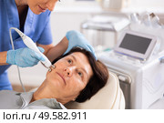 Elderly female client receiving hardware ultrasonic to revitalize and tighten facial skin at cosmetology clinic. Стоковое фото, фотограф Яков Филимонов / Фотобанк Лори