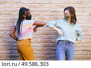 Multiethnic young women wearing masks greeting at each other with their elbows outdoors. Multiethnic young women wearing masks greeting at each other with their elbows. Стоковое фото, агентство Ingram Publishing / Фотобанк Лори