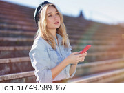 Blonde woman using her smartphone sitting on some city steps, wearing a denim shirt and black beret.. Blonde woman using a smartphone sitting on some city steps, wearing a denim shirt and black beret. Стоковое фото, агентство Ingram Publishing / Фотобанк Лори