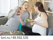 two pregnant women friends eating bad food at home. Стоковое фото, агентство Ingram Publishing / Фотобанк Лори