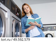 shot of a young woman reading a book in laundromat. Стоковое фото, агентство Ingram Publishing / Фотобанк Лори