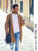 Young black man walking down the street carrying a briefcase and a smartphone. Cuban guy in urban background.. Young black man walking down the street carrying a briefcase and a smartphone. Стоковое фото, агентство Ingram Publishing / Фотобанк Лори