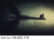 Depressed young man sitting alone isolated in a dark room, casting a shadow of a powerful guardian angel. Inner strength conceptual background. Stressed person introvert with an imaginary friend. Стоковое фото, агентство Ingram Publishing / Фотобанк Лори