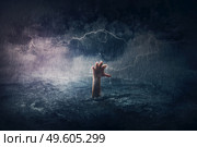 Arm drowning in the sea. Surreal and dramatic scene of person hand sinking in the ocean under a hurricane stormy weather. People need help in risk situations. Despair, depression and failure metaphor. Стоковое фото, агентство Ingram Publishing / Фотобанк Лори