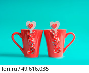 Two red tea cups with chocolate pralines and hearts at blue background. Valentines day and love concept. Front view. Стоковое фото, агентство Ingram Publishing / Фотобанк Лори