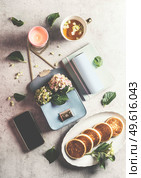 Feminine freelancer lifestyle. Pancakes, tea cup, scented candle,  smartphone, blue handbag with hydrangea and writing utensils on light grey concrete table. Top view. Стоковое фото, агентство Ingram Publishing / Фотобанк Лори