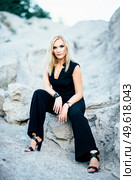 blonde girl in a black trouser suit with blue eyes on the background of a granite quarry from gray rubble. Стоковое фото, агентство Ingram Publishing / Фотобанк Лори