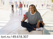 Hapy black woman using a smartphone, wearing her hair in braids. Typical African hairstyle.. Happy black woman using a smartphone outdoors, wearing her hair in braids. Стоковое фото, агентство Ingram Publishing / Фотобанк Лори