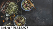 Bowls with Asian soup with cabbage, mushrooms, shiitake, garlic, chili and dumpling in traditional crockery with chopsticks on dark concrete table. Food banner with healthy ramen noodles. Top view. Стоковое фото, агентство Ingram Publishing / Фотобанк Лори