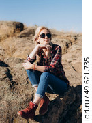 blonde girl with pigtails in a shirt, jeans, red shoes and black glasses on granite rocks. Стоковое фото, агентство Ingram Publishing / Фотобанк Лори