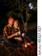 Young couple a guy and a girl in bright knitted hats stopped at a camping near the fire. Стоковое фото, агентство Ingram Publishing / Фотобанк Лори