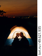 Young couple a guy and a girl in bright knitted hats stopped at a camping near the fire. Стоковое фото, агентство Ingram Publishing / Фотобанк Лори