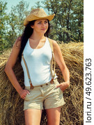 girl with black hair in beige wool coats and suspenders stands near the haystacks. Стоковое фото, агентство Ingram Publishing / Фотобанк Лори