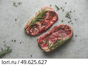 Raw marble black angus steak with rosemary and green pepper on grey concrete kitchen table. Top view. Стоковое фото, агентство Ingram Publishing / Фотобанк Лори