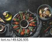 Marinated fried chicken wings with sauce and rosemary on dark plate at rustic black table with oil, spices and tablecloth. Top view with copy space. Стоковое фото, агентство Ingram Publishing / Фотобанк Лори