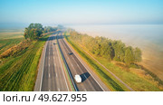 Sunny Magical autumn foggy morning. Aerial view of highway with cars. Asphalt road covered in fog. Early misty dawn. M1 magistaral in Belarus. Стоковое фото, агентство Ingram Publishing / Фотобанк Лори