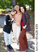 Positive young multiethnic female best friends in casual clothes smiling and looking at camera while cuddling in park on sunny day. Delighted young diverse ladies embracing and smiling in park. Стоковое фото, агентство Ingram Publishing / Фотобанк Лори