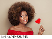 Beautiful portrait of an African girl with a heart shaped lollipop. Valentine’s Day. Symbol of love. Стоковое фото, агентство Ingram Publishing / Фотобанк Лори