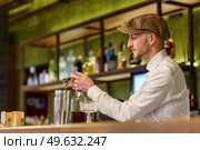 Bearded barman in white shirt and cap pouring liquor into shaker while preparing cocktail on counter in pub. Male barkeeper pouring alcohol into shaker. Стоковое фото, агентство Ingram Publishing / Фотобанк Лори