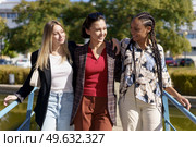 Cheerful multiracial female friends looking at each other while standing together on bridge over river in city on summer day. Positive diverse women on footbridge in city. Стоковое фото, агентство Ingram Publishing / Фотобанк Лори