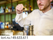 Soft focus of crop barkeeper in white shirt using pipette to add bitters to shaker while preparing cocktail during work in bar. Barman adding bitters to cocktail in a modern pub. Стоковое фото, агентство Ingram Publishing / Фотобанк Лори
