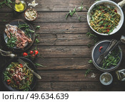 Green pasta on plates, ingredients and kitchen utensils with Parma ham, tomatoes, arugula, cheese and olive oil. Italian food background. Frame. Top view. Стоковое фото, агентство Ingram Publishing / Фотобанк Лори