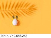 Easter scene with white eggs with rabbits ears over illuminating yellow background, palm shadows overlay. Easter scene with white eggs. Стоковое фото, агентство Ingram Publishing / Фотобанк Лори