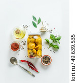 Pickled preserved yellow squash vegetables in glass jar on white background with flavoring ingredients: herbs, spices, oil and spoon. Top view. Стоковое фото, агентство Ingram Publishing / Фотобанк Лори