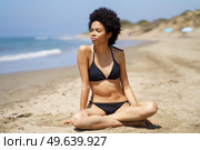 Relaxed black woman in bikini sitting on the sand of a tropical beach looking out to sea. African American girl tanning.. Relaxed black woman in bikini sitting on the sand of a tropical beach looking out to sea. Стоковое фото, агентство Ingram Publishing / Фотобанк Лори