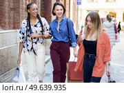 Group of optimistic multiethnic female friends with shopping bags strolling together on paved street near building after shopping in city. Content multiracial women with shopping bags. Стоковое фото, агентство Ingram Publishing / Фотобанк Лори