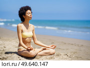 Black woman sitting on the beach doing mindfulness meditation in lotus position. Young female wearing yellow bikini.. Black woman sitting on the beach doing mindfulness meditation in lotus position. Стоковое фото, агентство Ingram Publishing / Фотобанк Лори