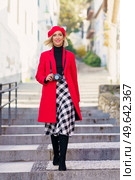 Full length of adult female with blond hair, in stylish outfit and beret smiling and looking at camera while walking on stairs on narrow street and photographing during holidays. Happy elegant lady walking downstairs on town street and smiling. Стоковое фото, агентство Ingram Publishing / Фотобанк Лори