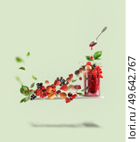 Flying cutting board with red jam jar, spoon and various berries:  currants, strawberries, raspberries, cherries, gooseberries and apricots at pale green background. Creative food levitation. Стоковое фото, агентство Ingram Publishing / Фотобанк Лори