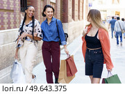 Group of cheerful multiracial female friends with shopping bags of purchases looking at each other while strolling on sidewalk near building in city. Smiling multiethnic women walking on street after shopping. Стоковое фото, агентство Ingram Publishing / Фотобанк Лори