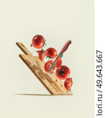 Flying sliced tomatoes, knife and wooden cutting board at pale beige background. Levitation ingredients with fresh vegetables. Creative food concept. Front view. Стоковое фото, агентство Ingram Publishing / Фотобанк Лори
