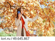 A young beautiful woman walks in the autumn park and talks on the phone. A girl with a smartphone takes photos in an autumn forest. Стоковое фото, агентство Ingram Publishing / Фотобанк Лори