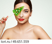 Beauty model girl eating Christmas tree shape lollipop.  Beautiful young woman with clean fresh skin. Girl beauty face care. Facial treatment. Cosmetology, beauty and spa. Red nails manicure. Стоковое фото, агентство Ingram Publishing / Фотобанк Лори