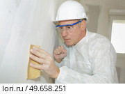 senior man wearing protection sanding interior wall for restoration. Стоковое фото, агентство Ingram Publishing / Фотобанк Лори