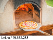 Delicious pizza from a hot outdoor stone oven with fire taken out with a food shovel . Стоковое фото, агентство Ingram Publishing / Фотобанк Лори