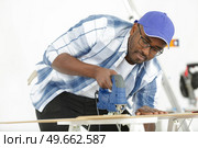 a man cutting wood block with fretsaw. Стоковое фото, агентство Ingram Publishing / Фотобанк Лори