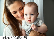 Little Baby With Ocean Eyes Held Lovingly by Mother Near Window. Стоковое фото, фотограф Aleksandr Golubev / Фотобанк Лори