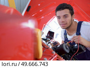 handsome young mechanic changing the cables in car. Стоковое фото, агентство Ingram Publishing / Фотобанк Лори