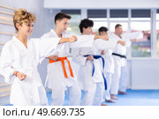 Preteen attendee of karate classes practicing kata standing in row with others. Стоковое фото, фотограф Яков Филимонов / Фотобанк Лори