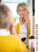 lady in her fifties applies skincare product to her face. Стоковое фото, агентство Ingram Publishing / Фотобанк Лори