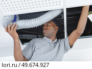 Man feeding ventilation hose above suspended ceiling. Стоковое фото, агентство Ingram Publishing / Фотобанк Лори