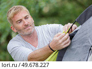 man putting up tent on camping trip. Стоковое фото, агентство Ingram Publishing / Фотобанк Лори